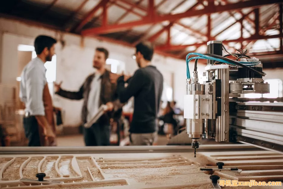Three men discussing work in a woodworking shop with CNC machinery in focus.