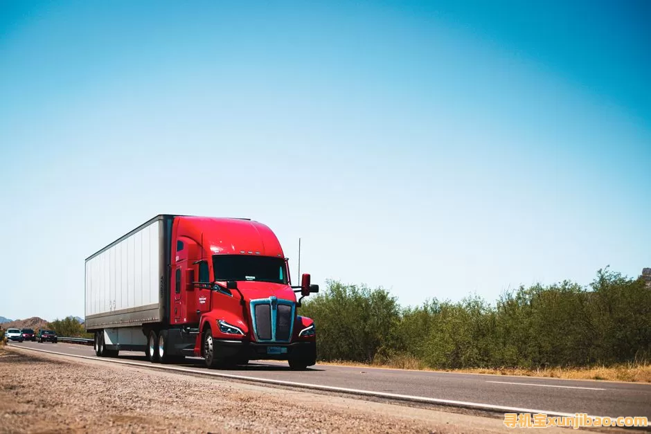 Vibrant red semi-trailer truck driving on an open highway under a clear blue sky.