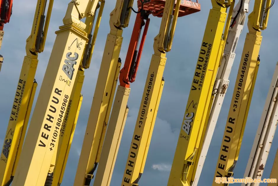 Multiple yellow boom lifts with text and numbers arranged against a blue sky.