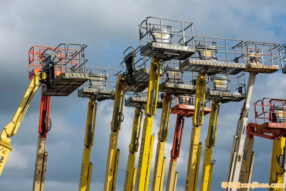 Multiple aerial work platforms with colorful booms reaching skyward against a cloud-dotted backdrop.