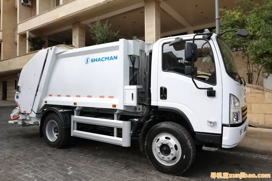 White Shacman garbage truck parked on a cobblestone street in an urban area, ready for waste collection.