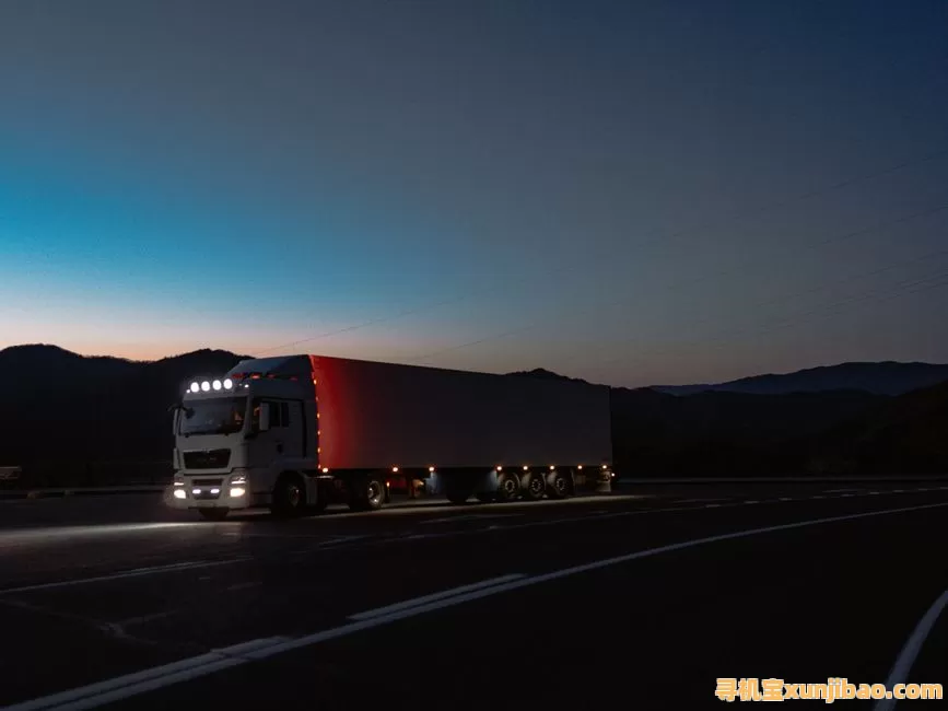 Large cargo truck travels on Altai road at night with mountains silhouetted against twilight sky.